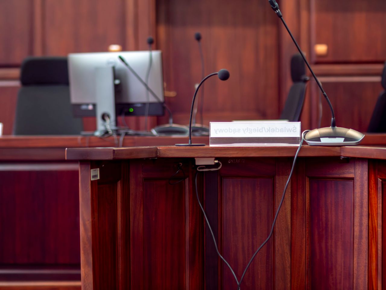 Close-up of a wooden podium with microphones in a Polish courtroom setting.